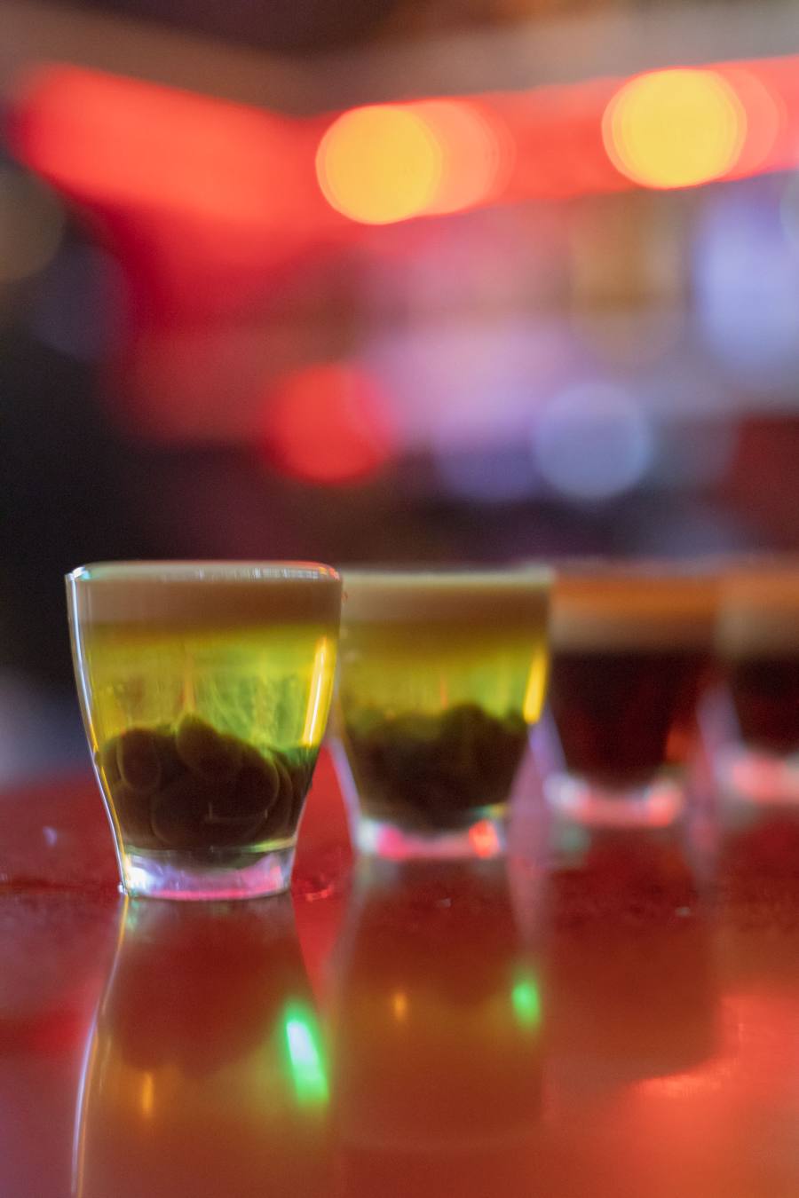Four small glasses of beer with green liquid in front of red lights