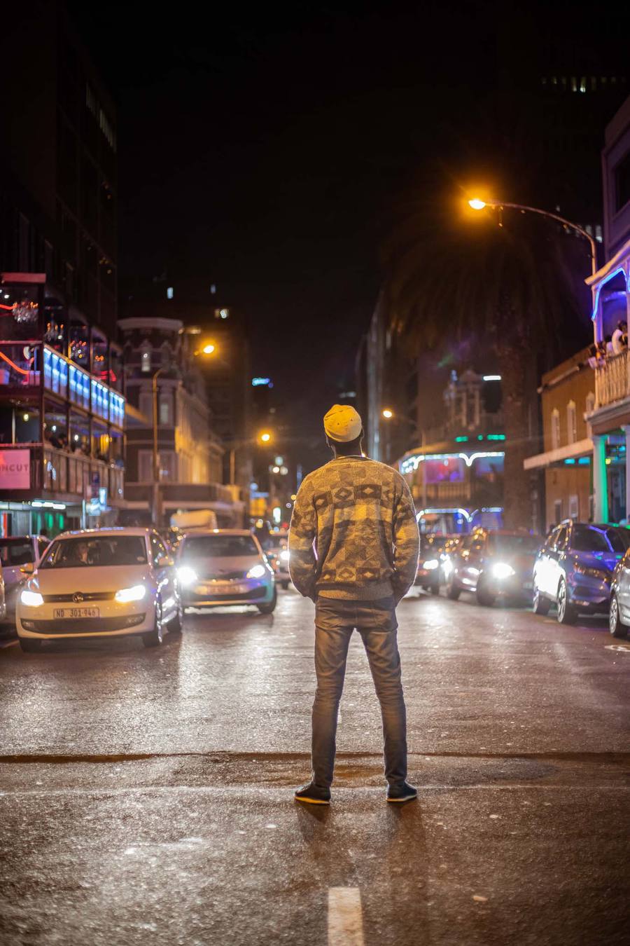 A man stands in the middle of a busy street at night, cars and buildings behind him.