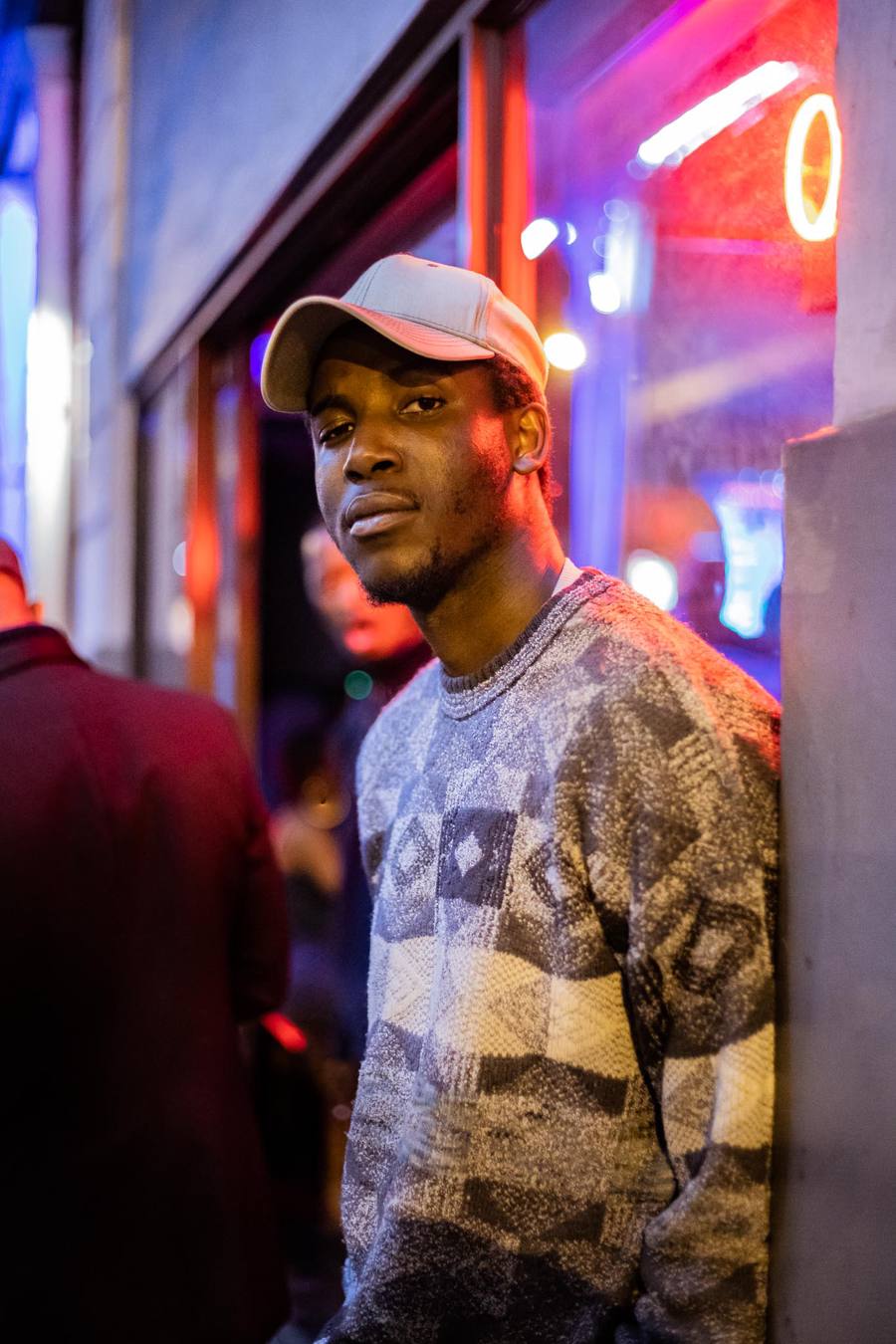Man in a cap and patterned jumper standing outside a building at night