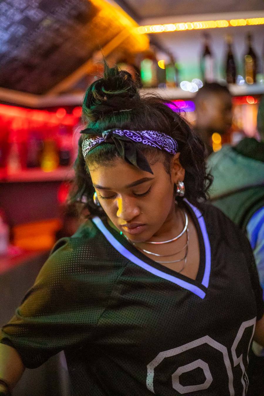 Woman with green hair and purple bandana looking down in a bar