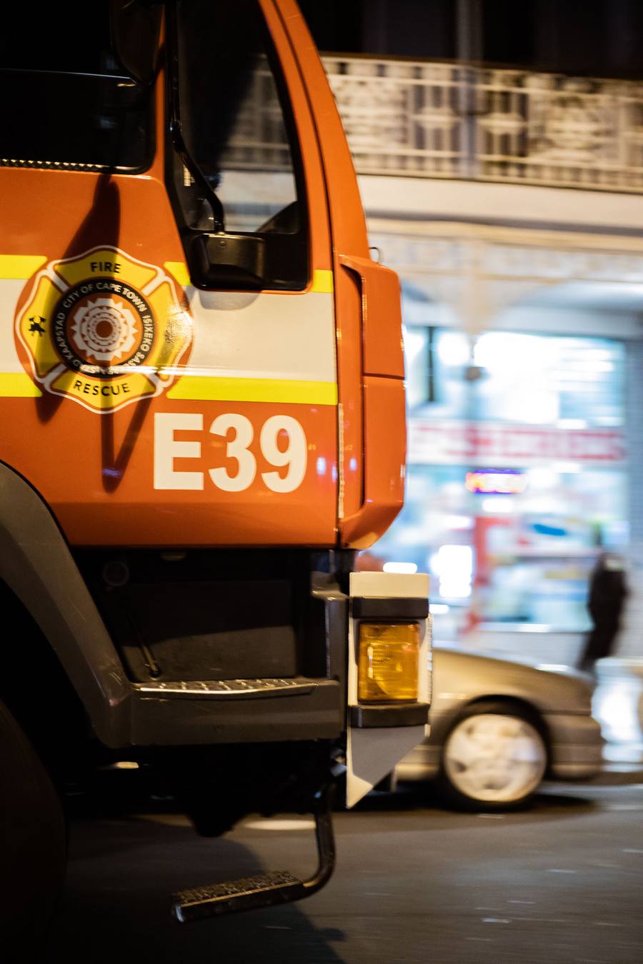 Fire truck E39 parked on a street, a car behind it, and a person walking in the background.