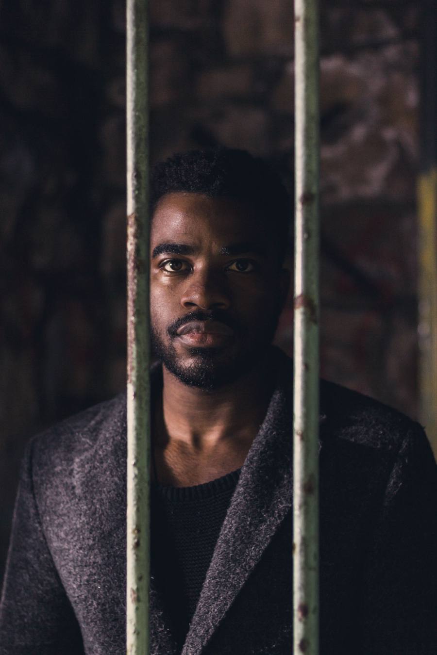 Man in a grey coat and black jumper looking through metal bars