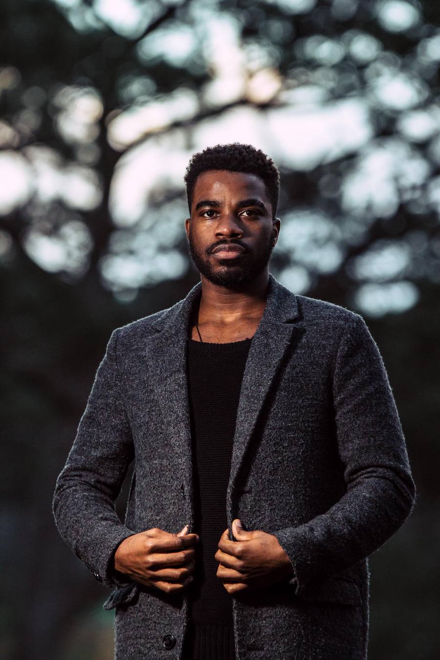 Man in a grey coat standing in a park with trees in the background