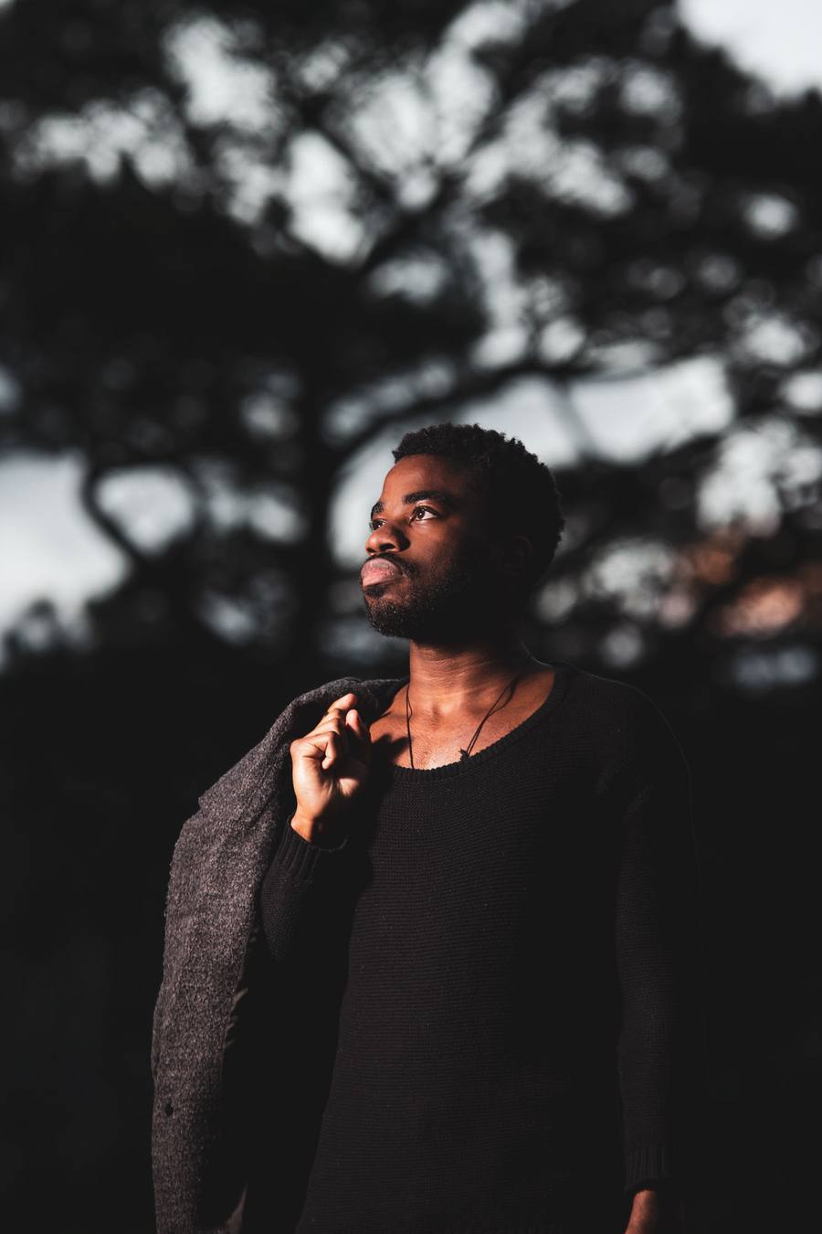 Man in black shirt and grey jacket standing in front of trees