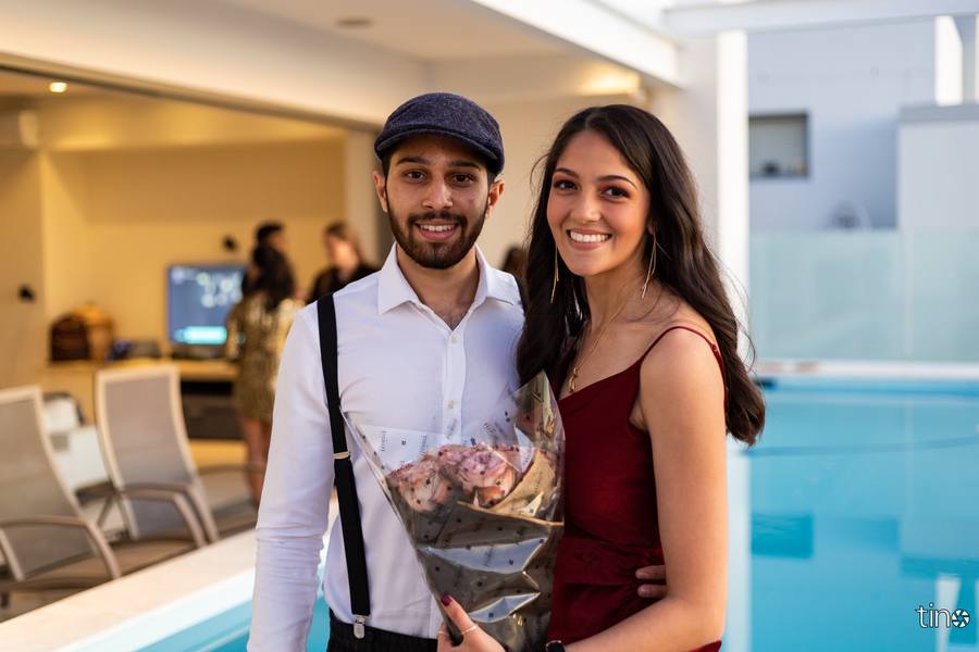 Couple smiling at camera, man holding bouquet, pool in background