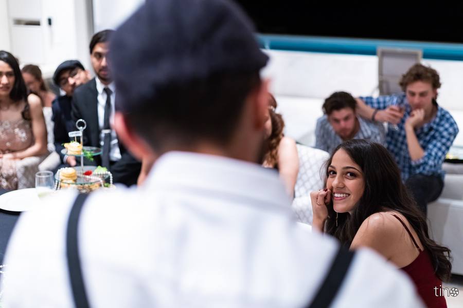 A woman smiles at a man while others sit around a table with food and drinks