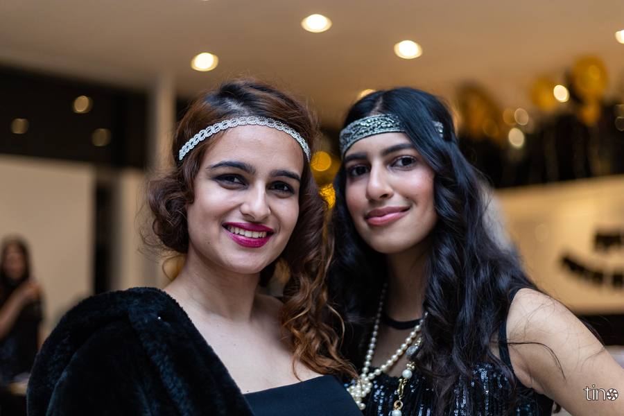 Two women in flapper-style outfits smile at the camera.