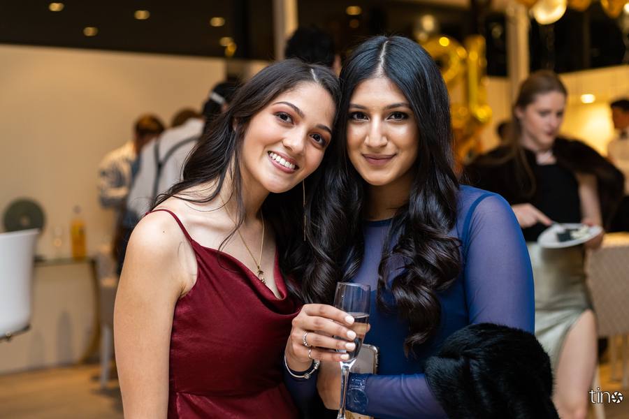 Two women smiling at the camera, one holding a glass of champagne