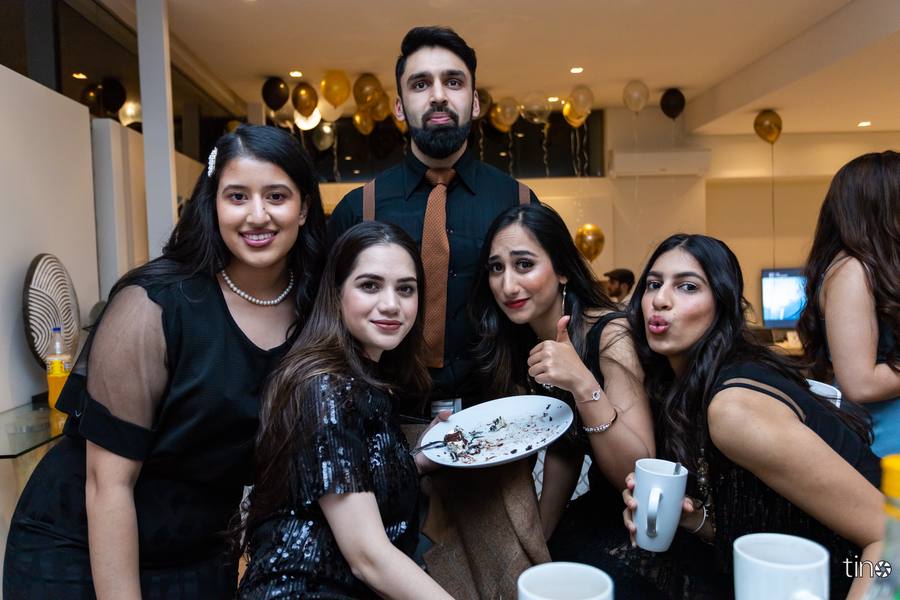 Five women and a man pose for a photo with a plate of cake and mugs