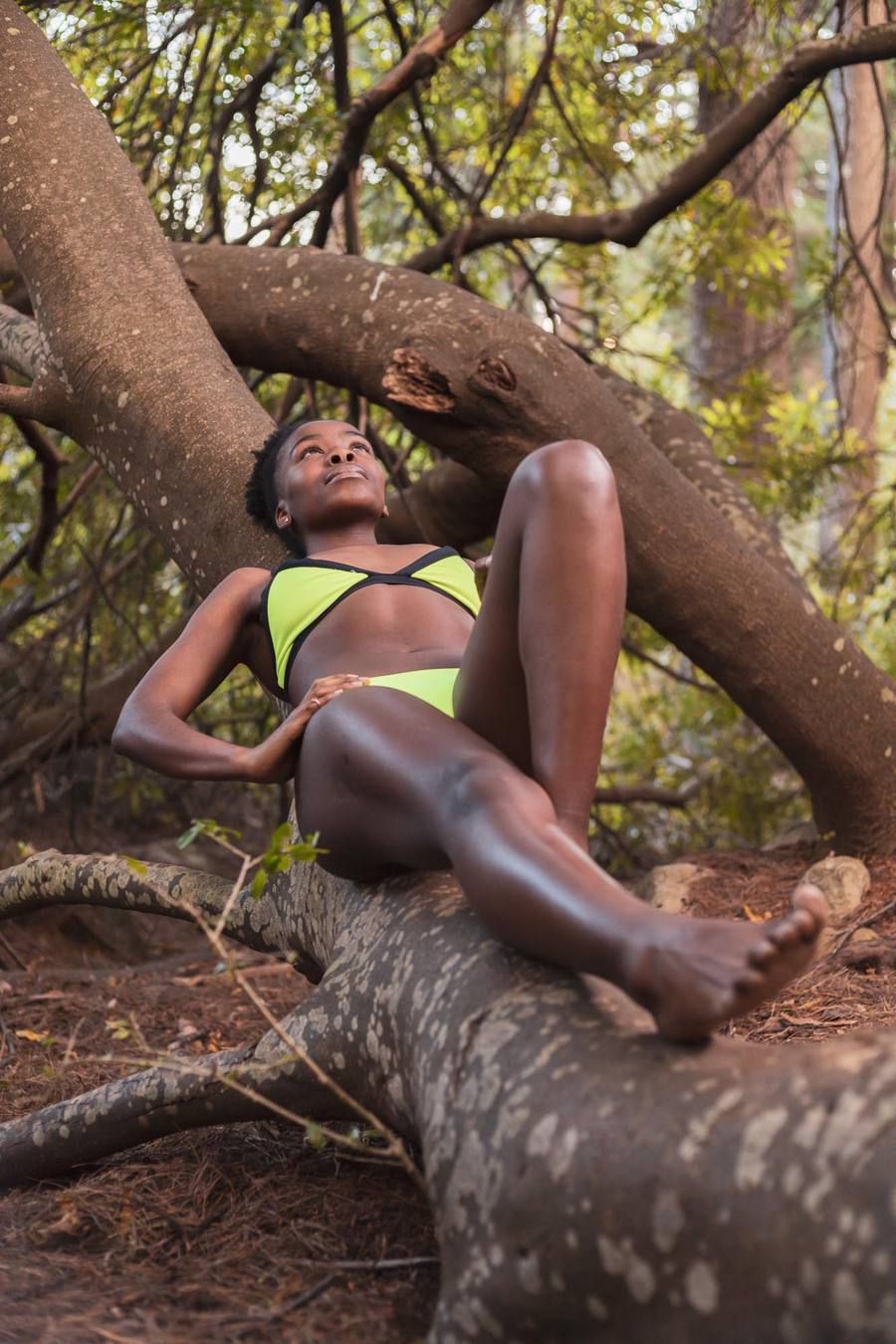 Woman in green bikini lying on tree branch in forest