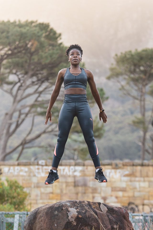 Woman in sports gear jumping over rock in outdoor setting
