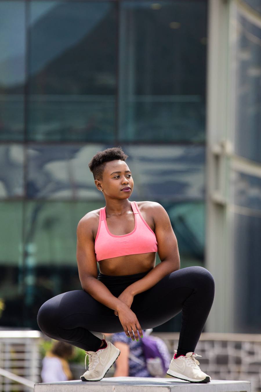 Woman in pink sports bra and black leggings squats on concrete platform