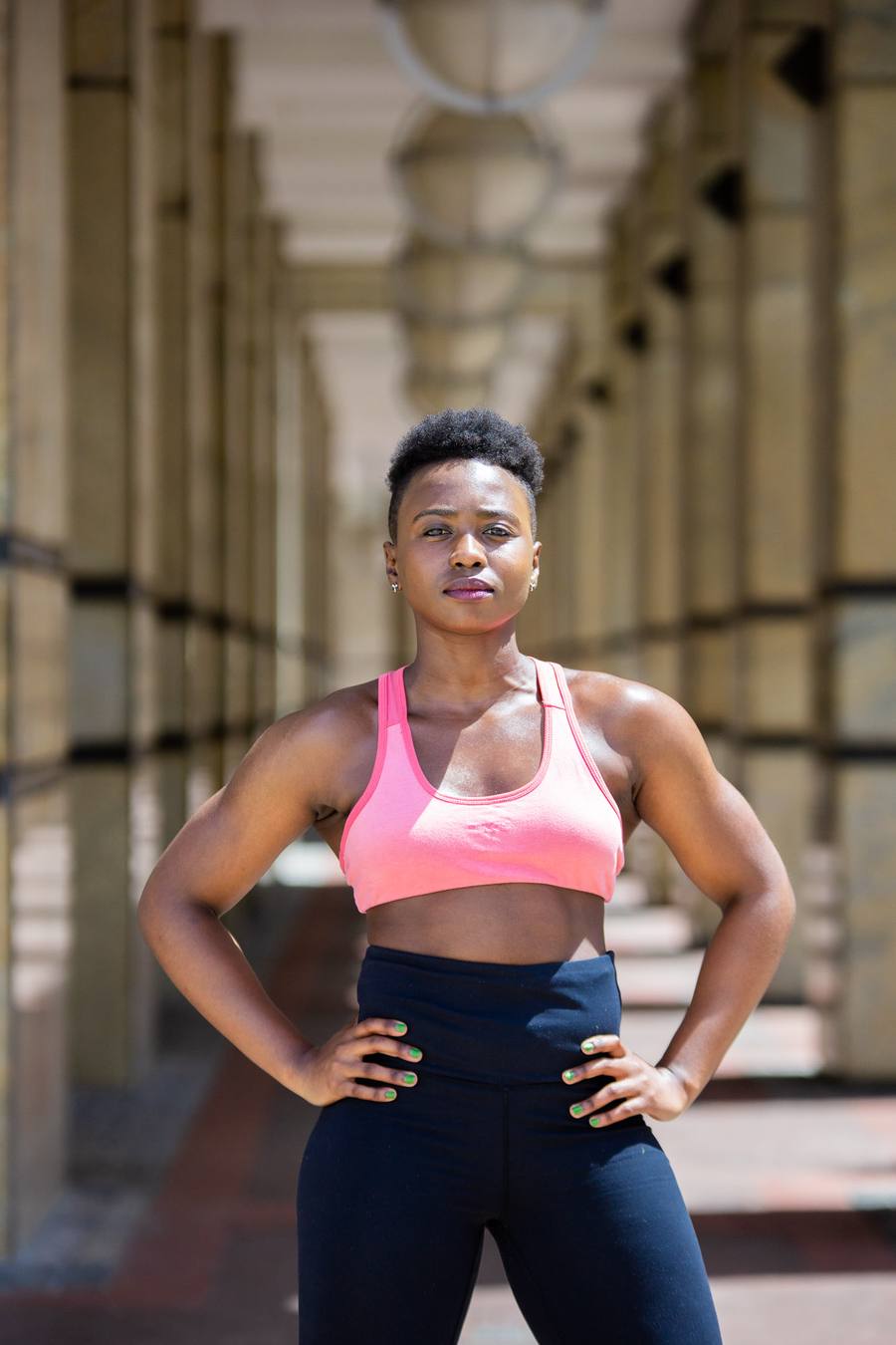 Woman in pink sports bra and blue leggings poses in a corridor
