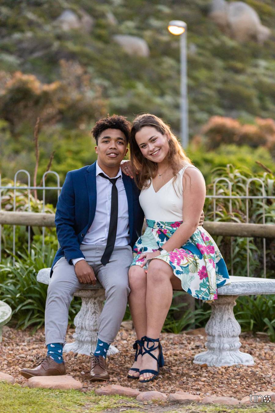 Couple sitting on a bench, smiling, with a garden in the background.