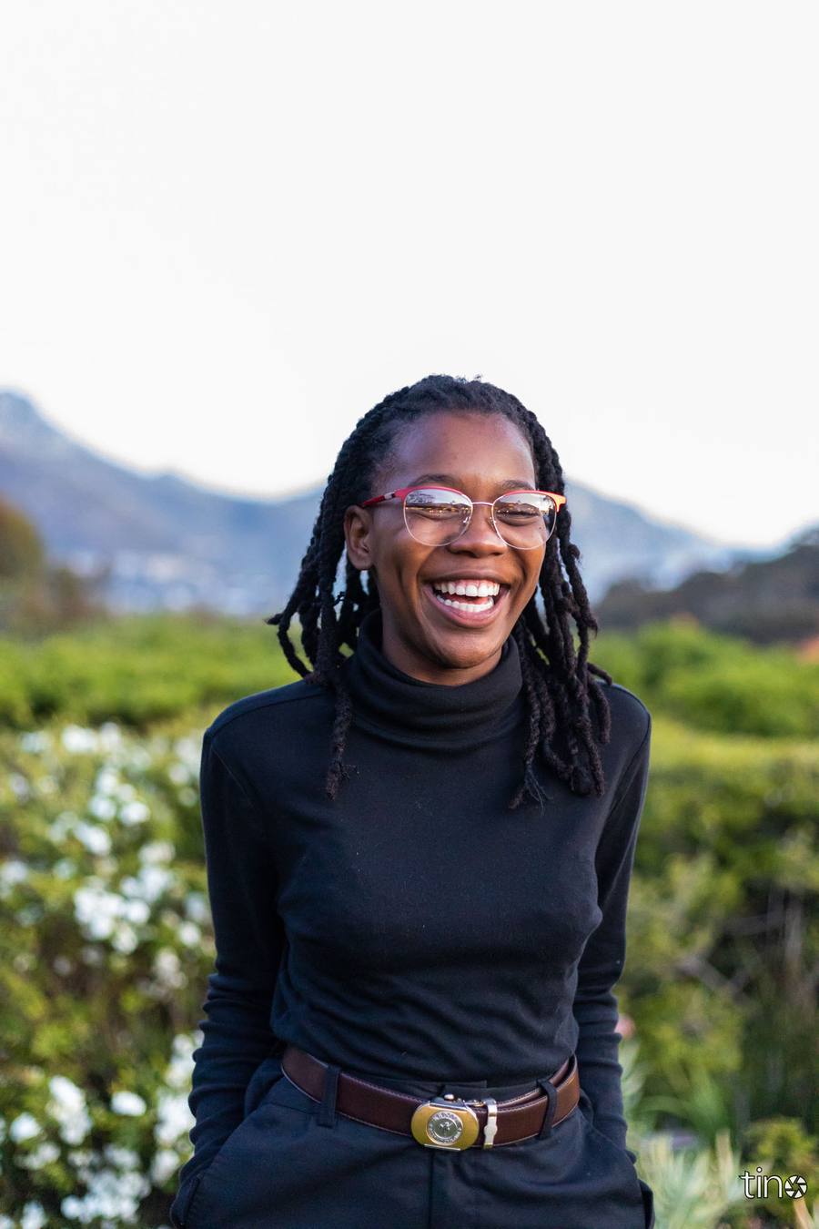 Woman with glasses and a black turtleneck smiling in a garden