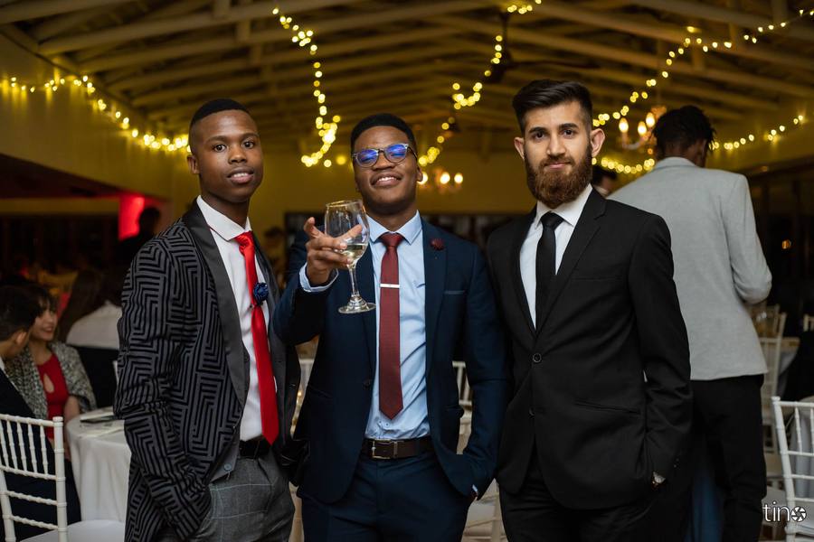 Three men in suits and ties, one holding a wine glass, smiling at camera