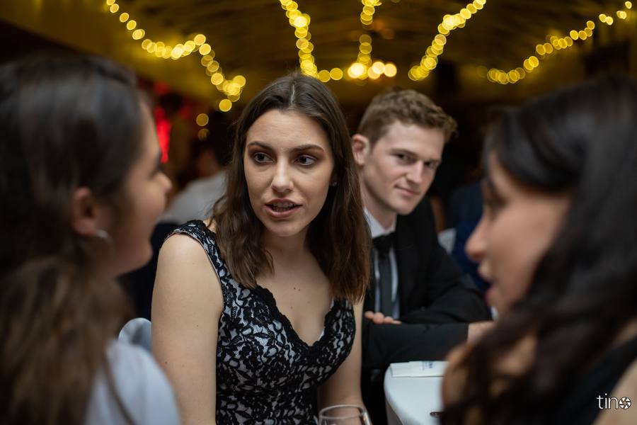 Three people sit at a table, two women facing each other, a man behind them