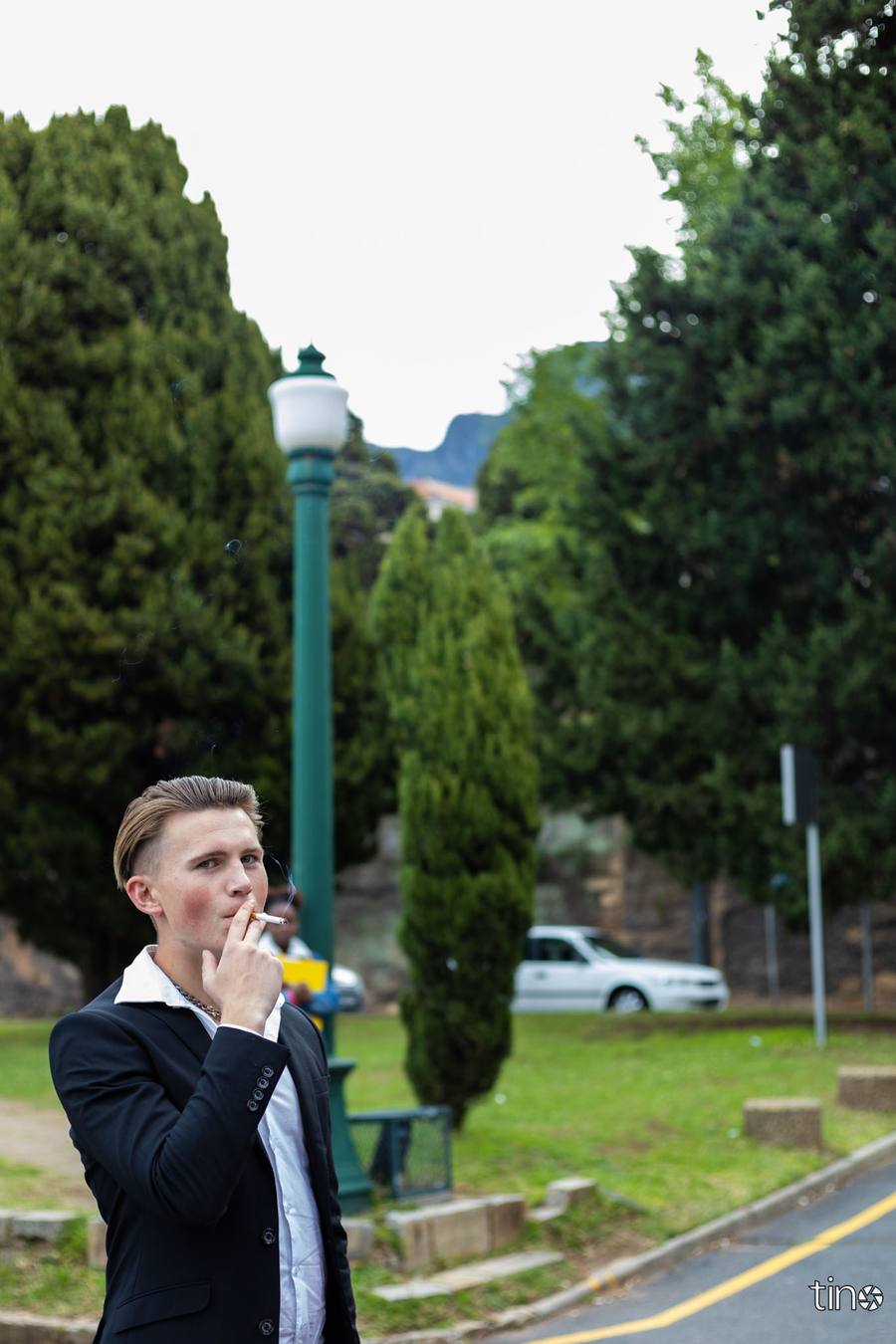 A man in a suit smokes a cigarette on a street corner.