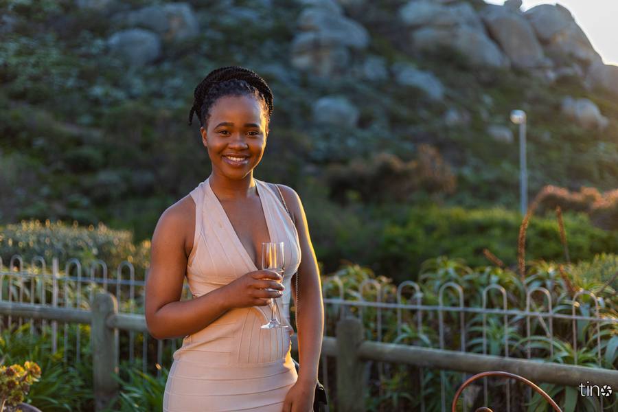 Woman in a sleeveless dress holding a glass of champagne in front of a fence