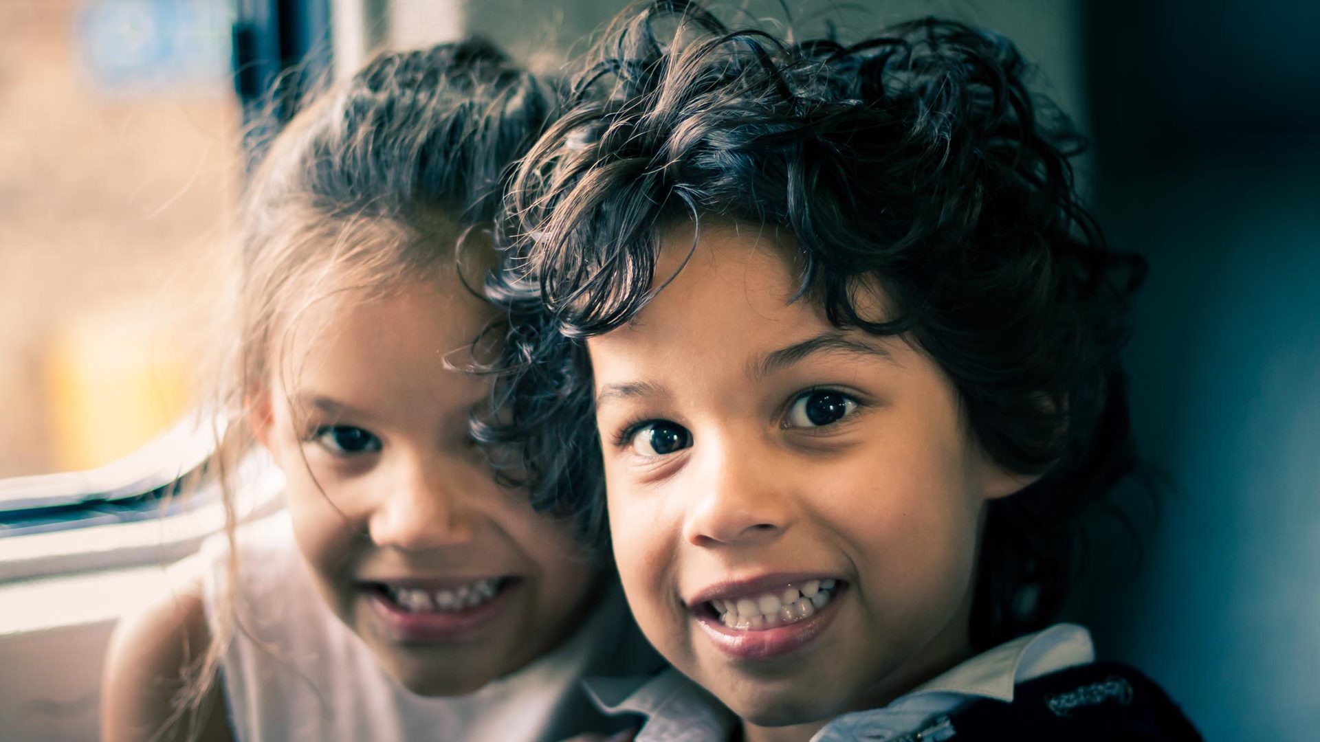Two children smiling at the camera, one with braces, seated in a vehicle.