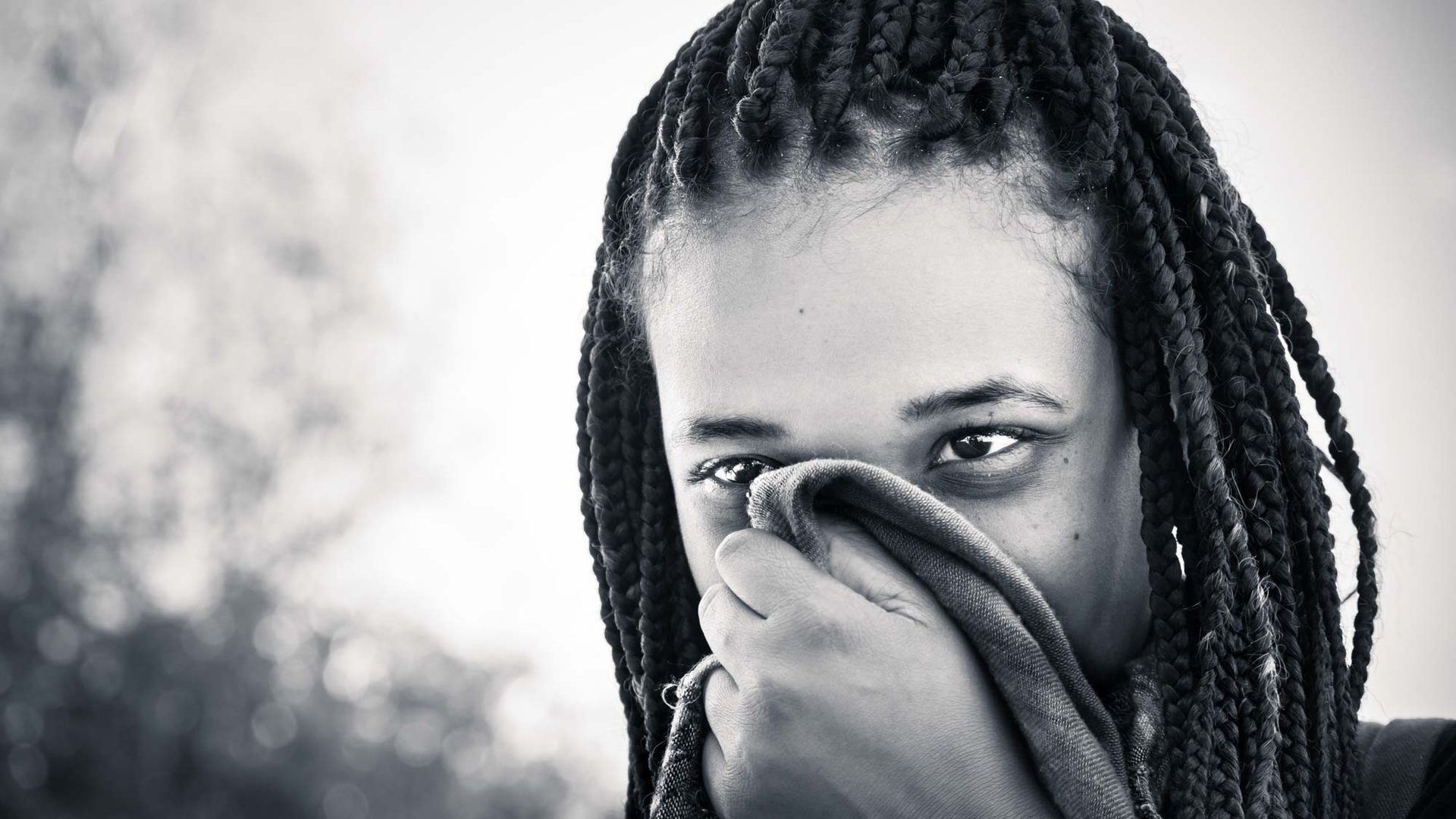 A woman with braided hair covering her face with a cloth